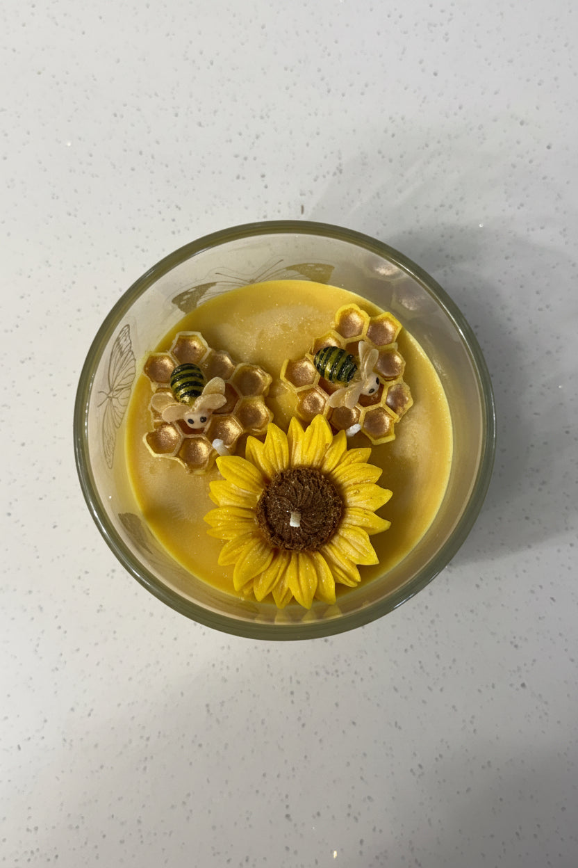 Vela aromatica de girasol con detalles de abeja y panal, hecha a mano, presentada en empaque elegante para regalo.